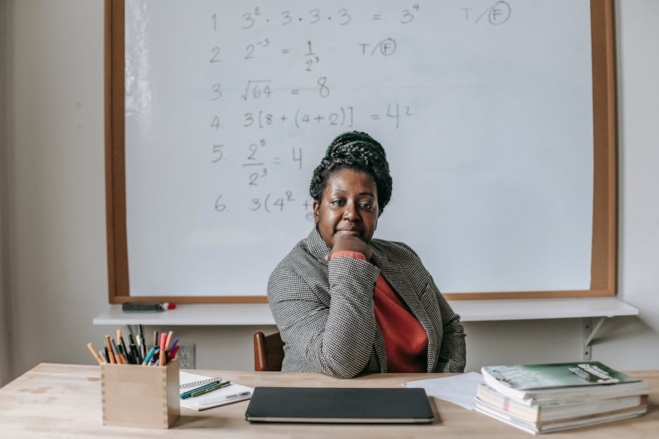 African American female teacher in formal clothes sitting at table with books and laptop and looking at camera